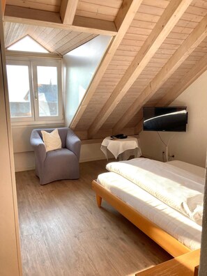 A small, sloped-roofed room with a bed, a chair, a table, and a TV mounted on the wall. - Rossli Hurden (Freienbach)