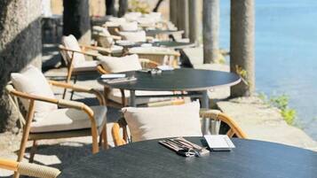 Un espace extérieur aménagé avec des tables rondes et des chaises en osier, offrant une vue sur un plan d’eau.