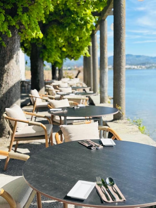 An outdoor seating area with round tables and wicker chairs, overlooking a body of water. - Rossli Hurden (Freienbach)