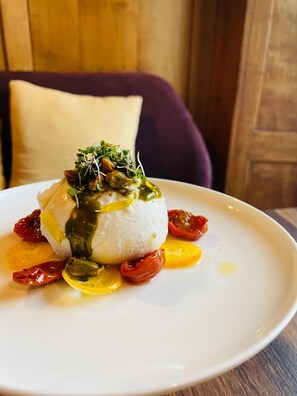 A white plate with a white spherical food item, garnished with green leaves and a drizzle of green sauce, surrounded by sliced vegetables. - Rossli Hurden (Freienbach)