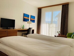A hotel room with two beds, a desk with a television, a chair, and artwork on the wall. - Rossli Hurden (Freienbach)