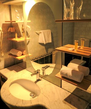 A bathroom with a sink, mirror, towel rack, and shelves with toiletries. - Hotel Consul (Split)