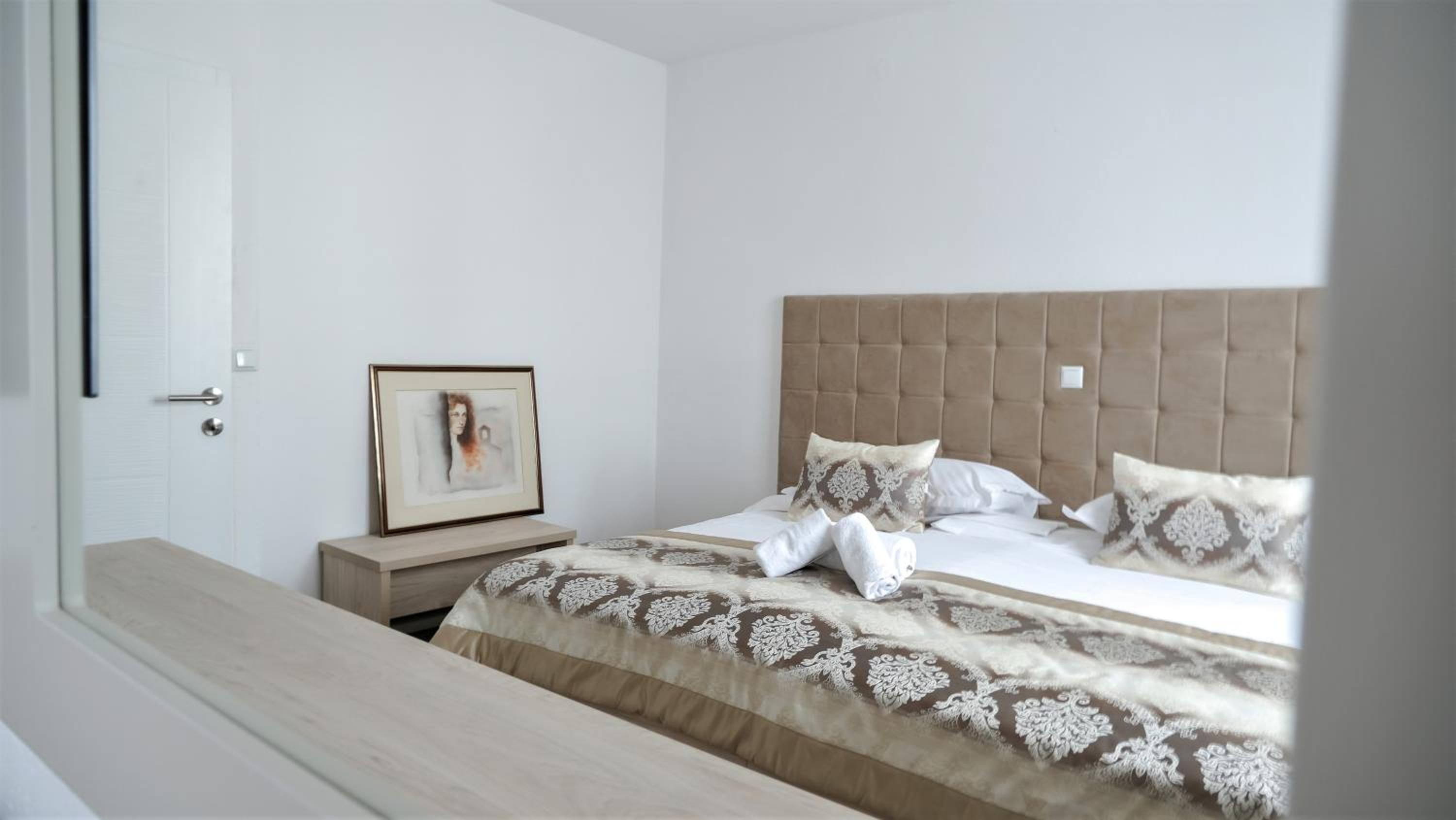 A bedroom with a bed, a nightstand, a framed picture, and a window.