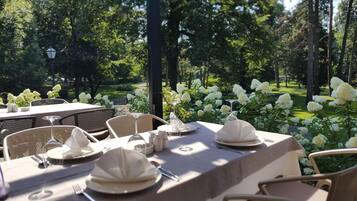 An outdoor dining area with tables set for a meal, surrounded by lush greenery and white flowers.