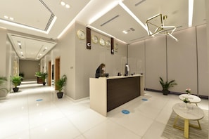 A hotel reception area with a reception desk, clocks, and potted plants. - Saray Deluxe Hotel Apartments (Abu Dhabi)
