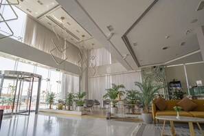 Un vestíbulo amplio con un diseño moderno, que incluye una zona de estar con sofás y sillones, un separador de vidrio y una variedad de plantas en macetas.