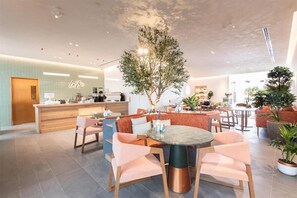 A modern hotel lobby with a central seating area, a reception desk, and a dining space. - Saray Deluxe Hotel Apartments (Abu Dhabi)