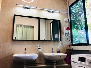A bathroom with two sinks, a mirror, a window, and a Panasonic washing machine. - Capsulepod@aljunied (Singapore)