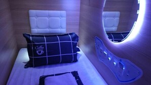 A compact room with a bed, a pillow with a coffee cup design, a small table, and a wall-mounted mirror. - Capsulepod@aljunied (Singapore)