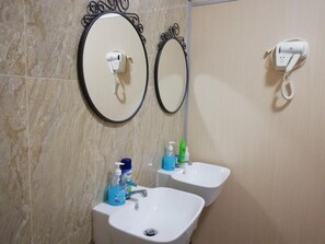 A bathroom with two sinks, a mirror, and a hairdryer on the wall. - Capsulepod@aljunied (Singapore)