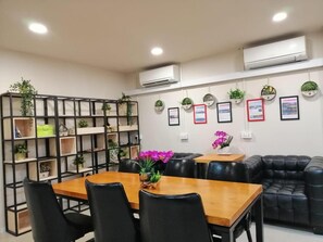 A conference room with a wooden table, black chairs, a black leather couch, and shelves with plants. - Capsulepod@aljunied (Singapore)