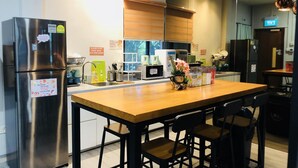 A modern kitchen with a stainless steel refrigerator, a wooden dining table with four chairs, and a microwave. - Capsulepod@aljunied (Singapore)