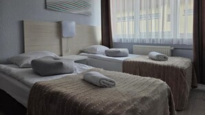 A hotel room with two beds, a headboard, a wall-mounted light, and a window with curtains. - Noclegi Gwardia (Koszalin)