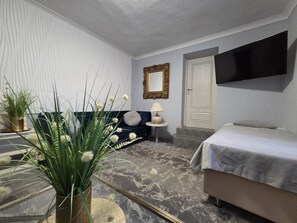 A hotel room with a bed, a sofa, a TV mounted on the wall, a small table with a lamp, and a potted plant. - Noclegi Gwardia (Koszalin)