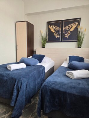 A hotel room with two beds, each with a blue bedspread and white pillows, a wooden wardrobe, and two framed butterfly artworks on the wall. - Noclegi Gwardia (Koszalin)