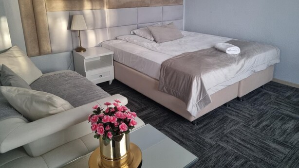 A hotel room with a bed, bedside table, lamp, and a small table with a vase of flowers. - Noclegi Gwardia (Koszalin)