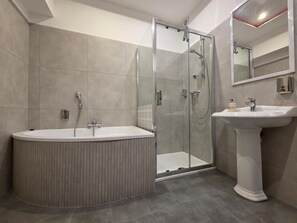 A modern bathroom with a freestanding bathtub, a glass-enclosed shower, and a pedestal sink. - Noclegi Gwardia (Koszalin)