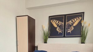 A hotel room with two beds, each with a blue bedspread and white pillows, a wooden wardrobe, and two framed butterfly artworks on the wall. - Noclegi Gwardia (Koszalin)