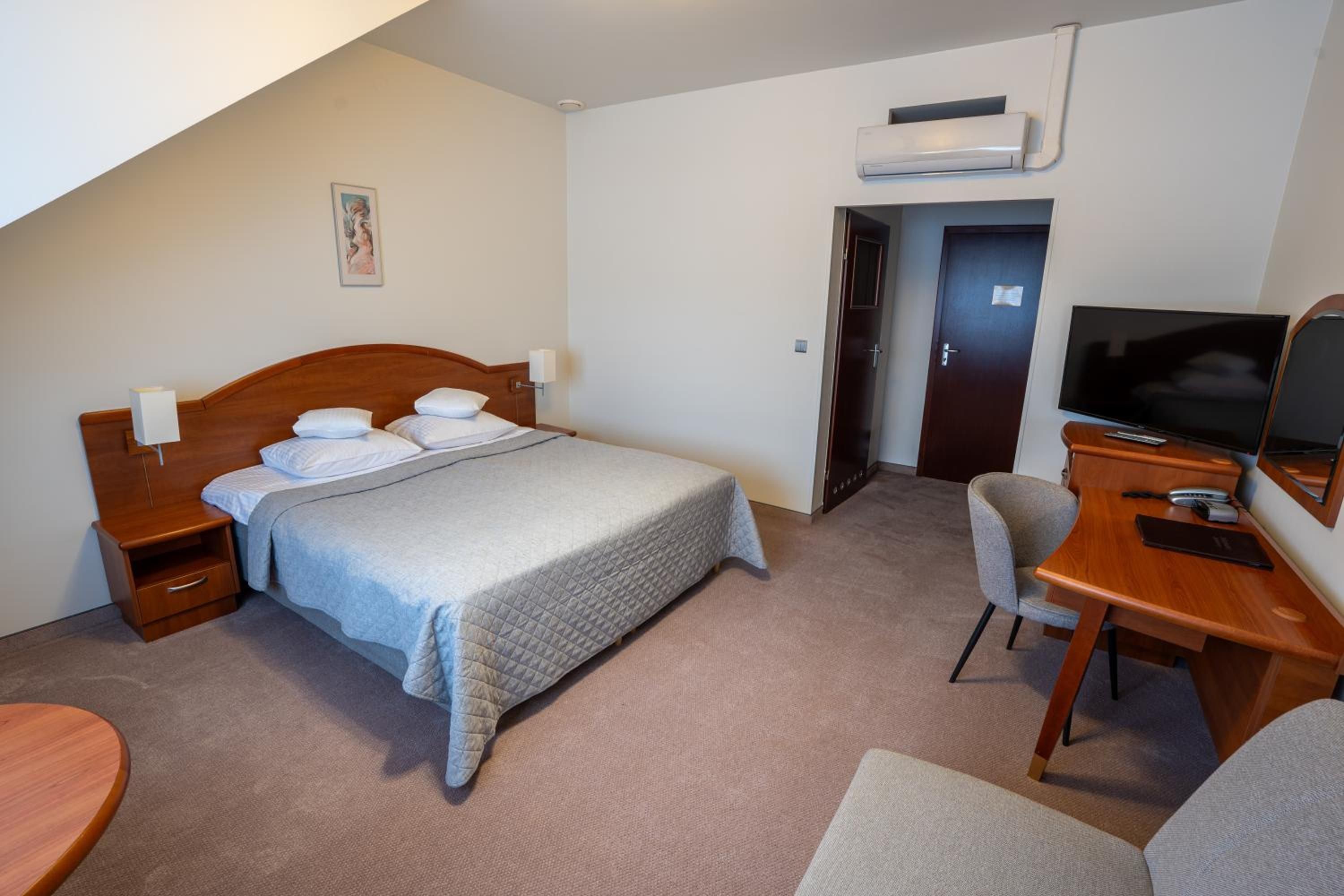 Een hotelkamer met een bed, nachtkastjes, een bureau met stoel, een televisie en een airconditioning.