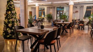 A spacious dining area with multiple tables and chairs, a Christmas tree, and potted plants. - Hotel Szelcow (Lesko)