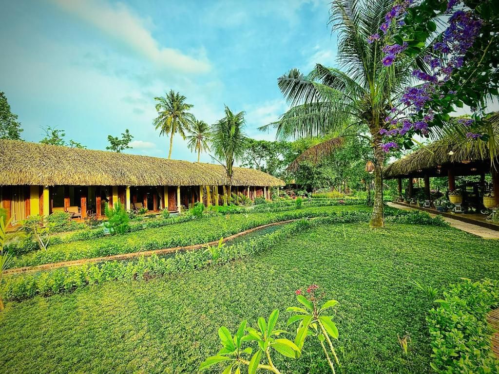 A resort with thatched-roof huts, a well-maintained garden, and palm trees.