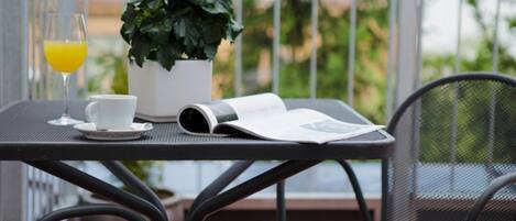 Una mesita con una planta en maceta, un vaso de zumo de naranja, una taza y una revista en un balcón.