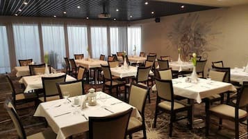 Uma sala de jantar de hotel com várias mesas postas, cadeiras e um grande mural decorativo.