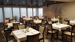 Comedor de hotel con varias mesas dispuestas para comer, sillas y un amplio mural decorativo.