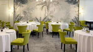 Comedor con mesas redondas, sillas verdes y un mural de palmeras en la pared.