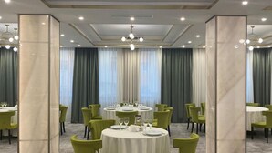 Un comedor de hotel con mesas redondas, sillas verdes y una araña.