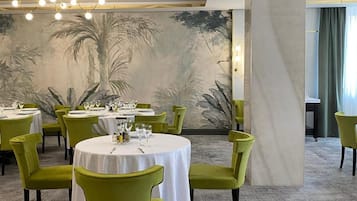 A dining area with round tables, green chairs, and a large mural on the wall.
