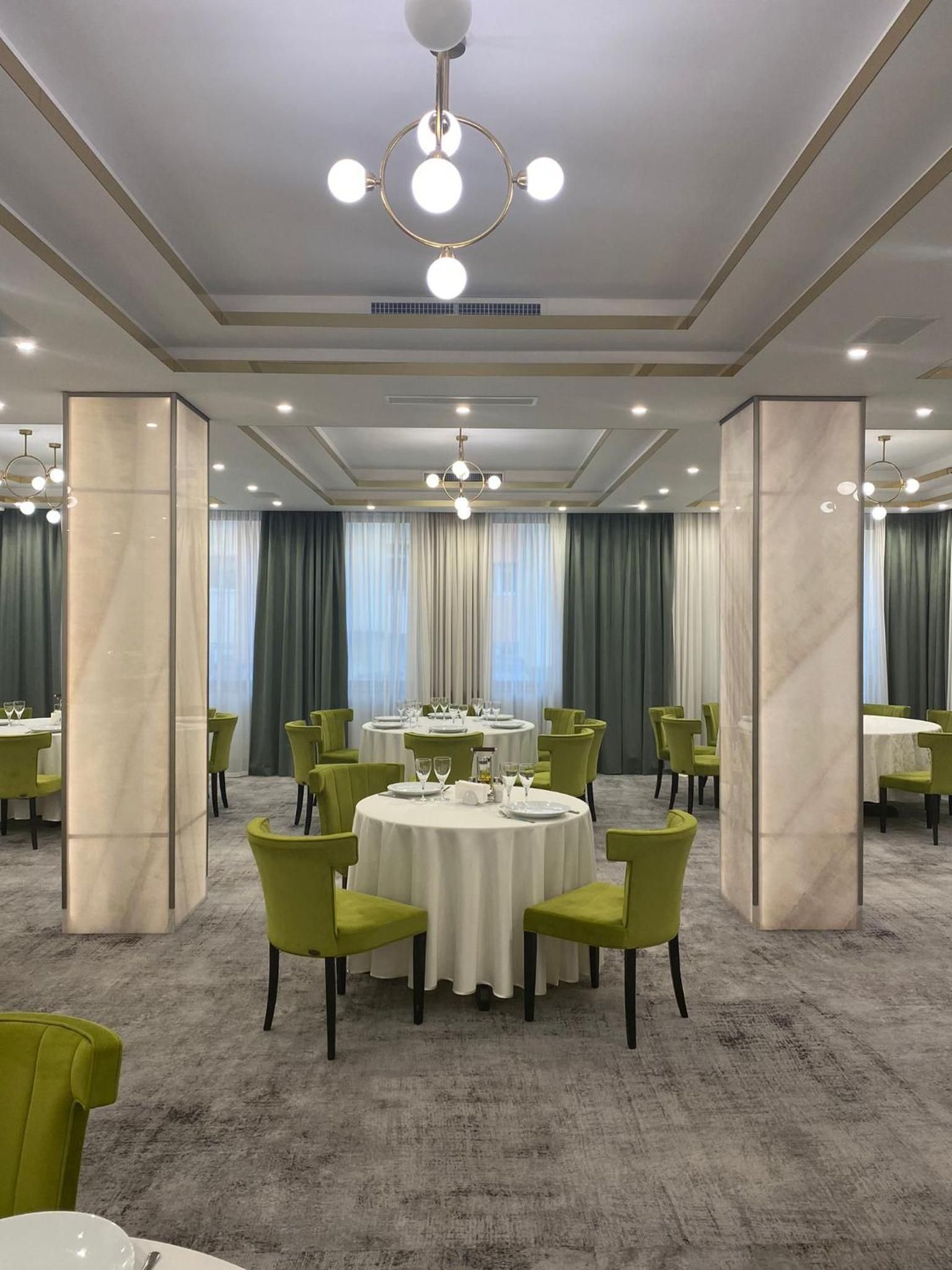 A hotel dining area with round tables, green chairs, and a chandelier.