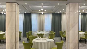 A hotel dining area with round tables, green chairs, and a chandelier.