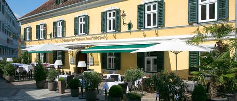 A yellow building with green shutters and outdoor seating.