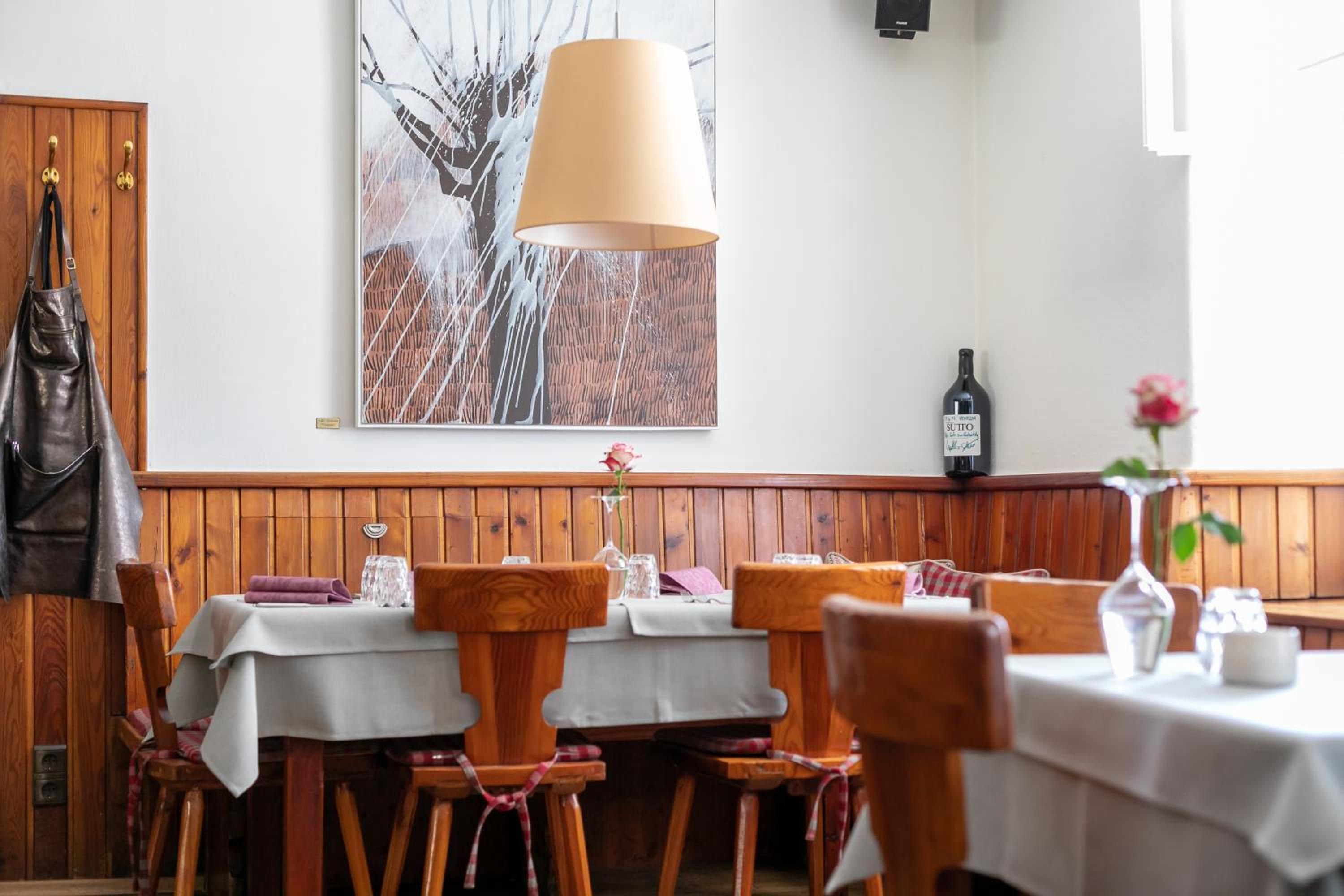 Ein Restaurantinnenraum mit Holzwänden, einem großen Gemälde, einem Tisch mit weißer Tischdecke und einer Weinflasche an der Wand.