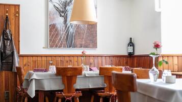 Ein Restaurantinnenraum mit Holzwänden, einem großen Gemälde, einem Tisch mit weißer Tischdecke und einer Weinflasche an der Wand.