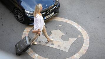 A person walking with a suitcase on a paved area with a car in the background.