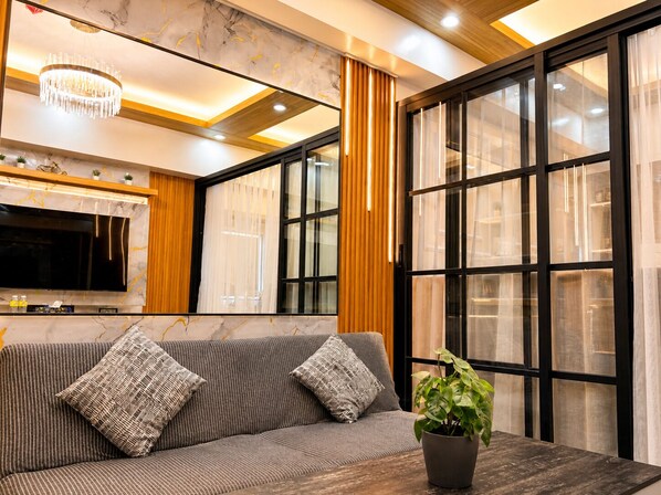 A modern living room with a sofa, TV, and a potted plant. - Luxury Stay for Less • Cozy Vibes + Epic Sunsets (Pasay City)