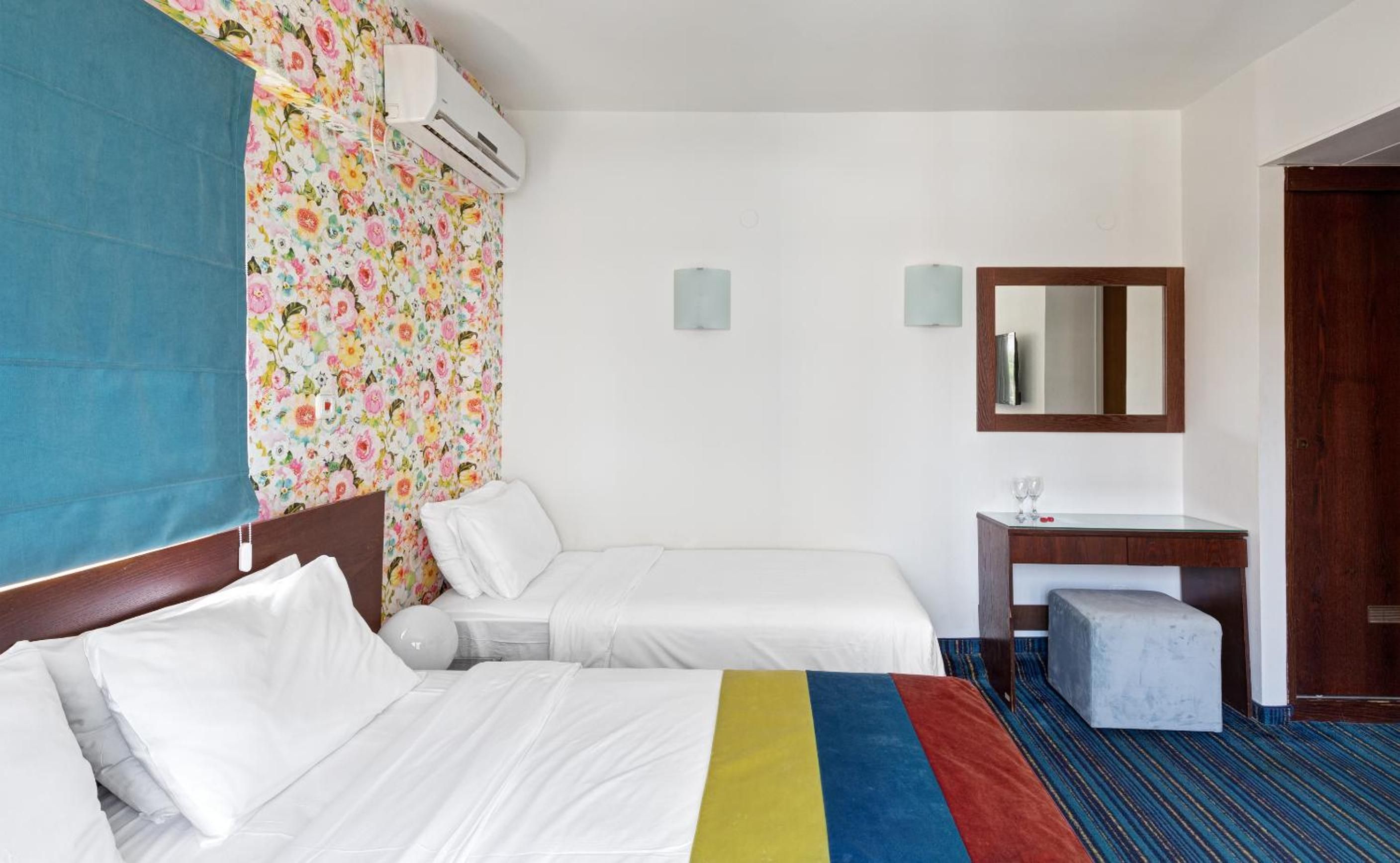 Habitación de hotel con dos camas, un escritorio con silla, un espejo, equipo de aire acondicionado y ventana con vistas.