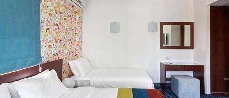 Habitación de hotel con dos camas, un escritorio con silla, un espejo, equipo de aire acondicionado y ventana con vistas.