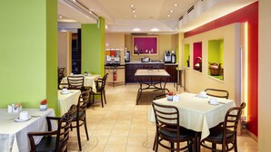 Een restaurant met meerdere tafels en stoelen, een toonbank met een koffiemachine, en een muur met ingelijste foto's.