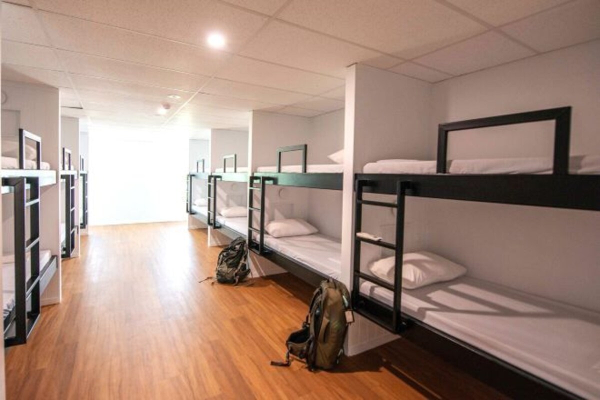 A dormitory room with bunk beds, wooden flooring, and a backpack on the floor.
