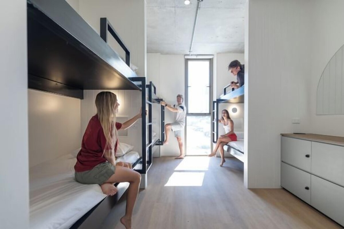 A dormitory-style room with bunk beds, a kitchenette, and a bathroom.