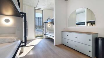 Quarto de hotel moderno com beliches, um espelho grande, cômoda de madeira e vista para o exterior.