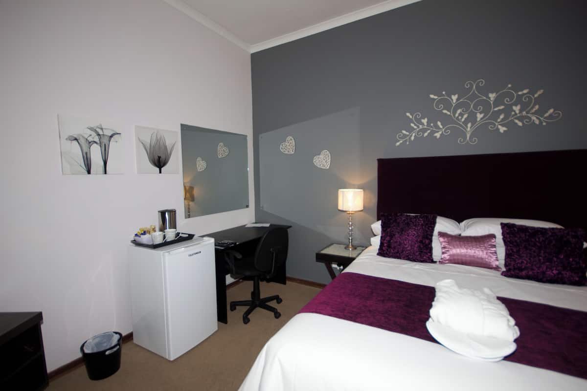 A hotel room with a bed, desk, chair, and a trash bin.