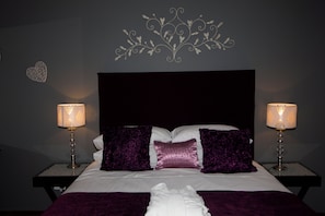 A bed with a headboard, two bedside tables with lamps, and decorative wall art. - Loerie Lodge (Phalaborwa)