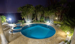 A swimming pool with a circular design, surrounded by palm trees and outdoor seating. - Loerie Lodge (Phalaborwa)