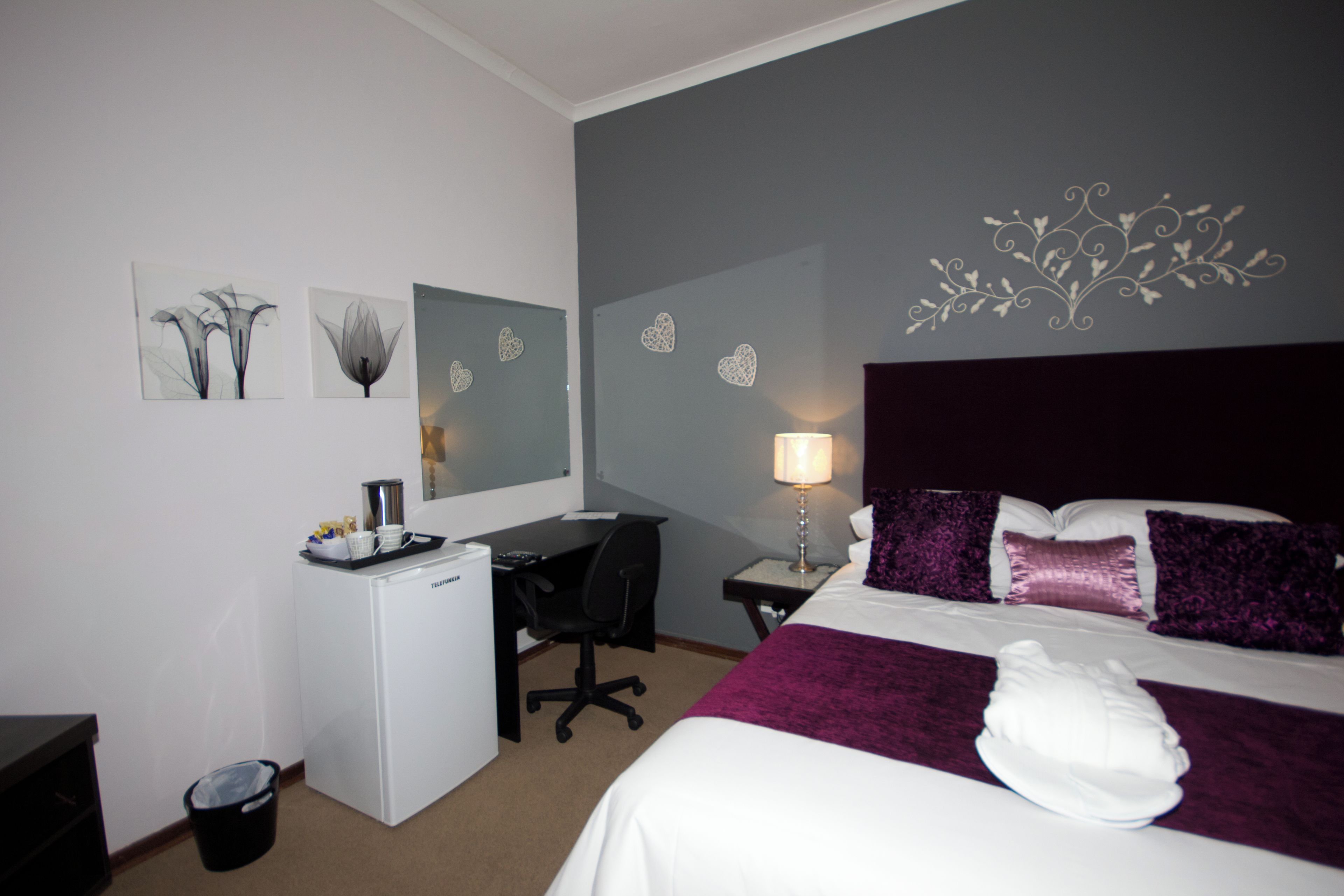 A hotel room with a bed, desk, chair, and a trash bin.