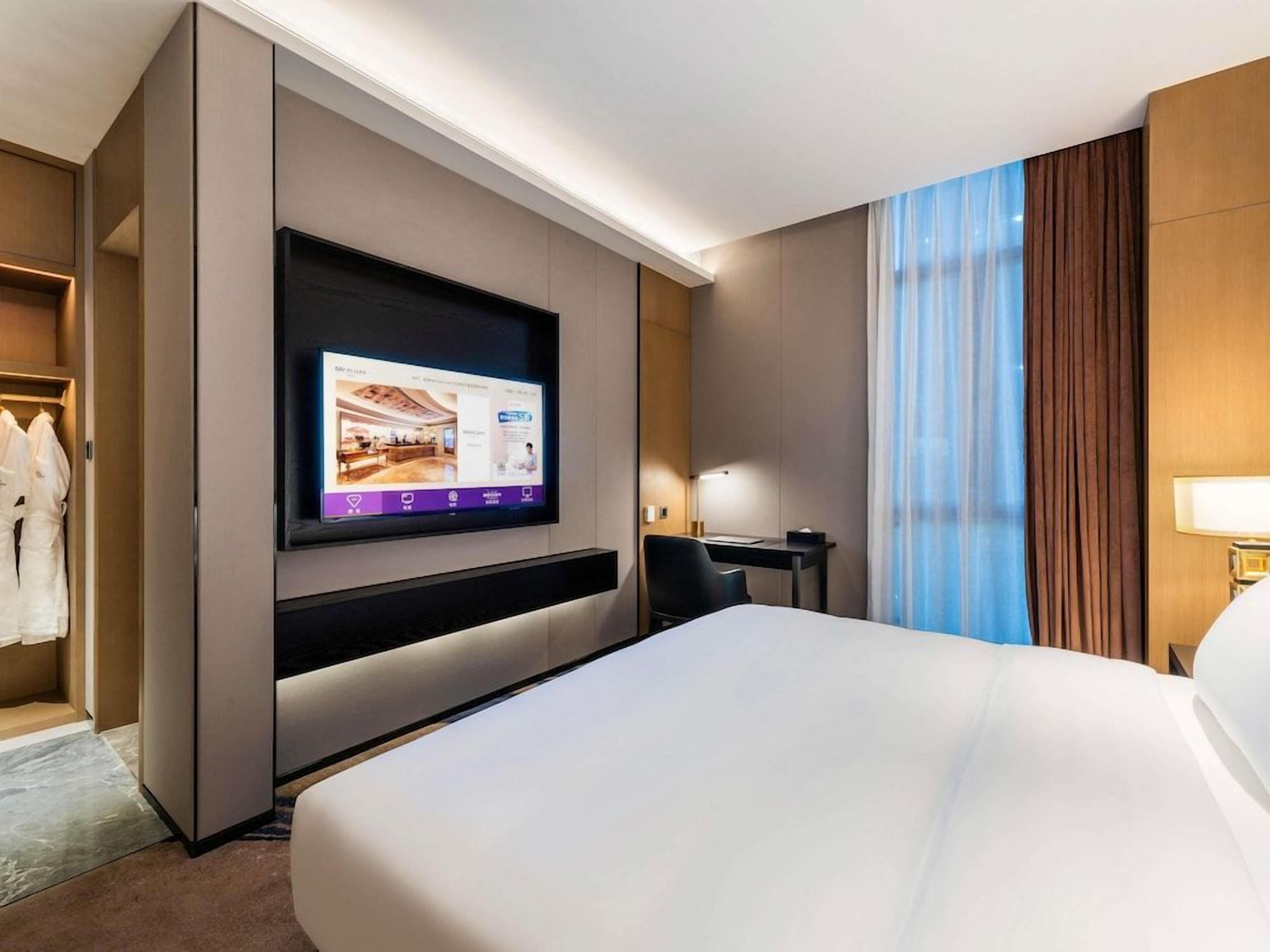 A hotel room with a large bed, a flat-screen TV mounted on the wall, a desk, and a chair.