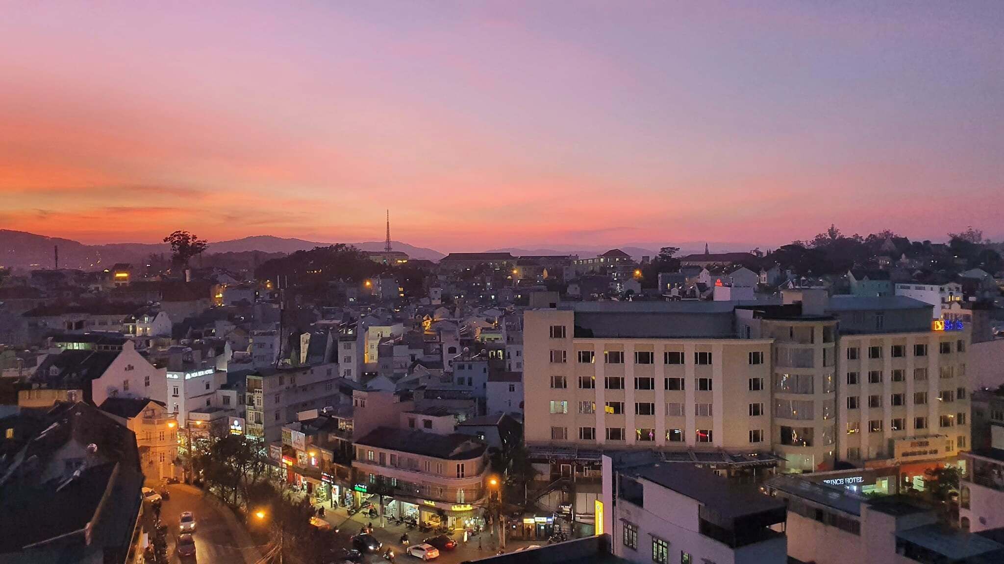 Une vue sur une ville au crépuscule, avec des bâtiments, un hôtel imposant et une montagne en arrière-plan.
